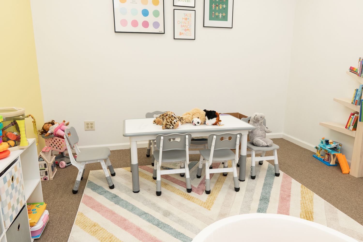 A bright playroom with white furniture, a striped rug, and toys scattered around.