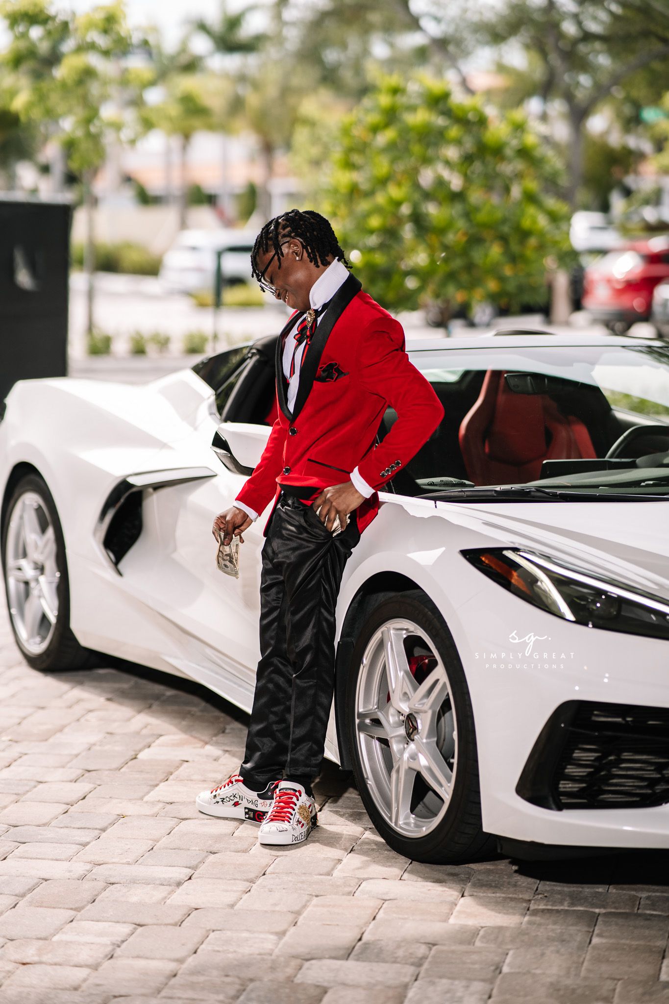 Sharp dressed person in red blazer poses next to white luxury sports car.