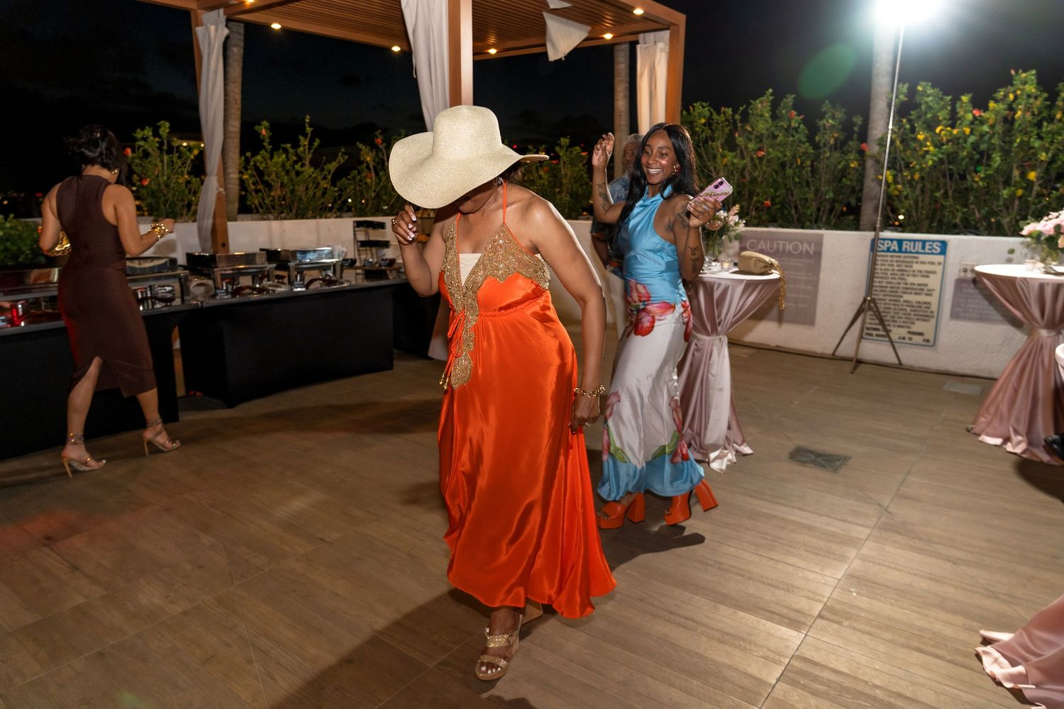 People dancing and celebrating at an outdoor party under a covered patio area.