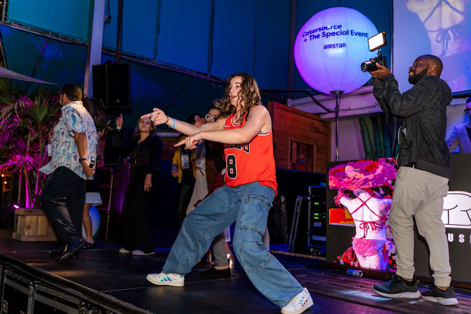 A performer dances energetically on stage under purple lighting at an event.