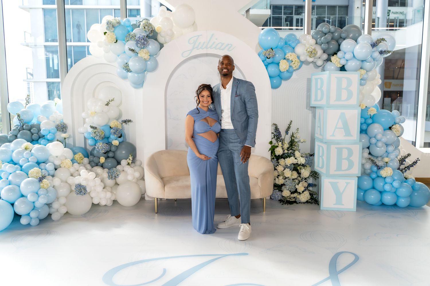 Couple posing in front of blue and white balloon arch at baby celebration.
