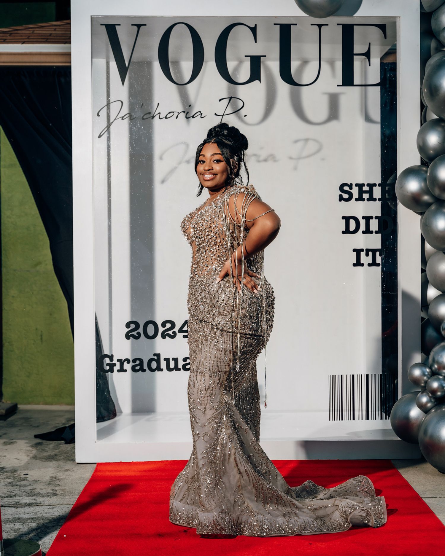 Graduate poses in sparkling beaded gown in front of custom Vogue magazine cover backdrop.