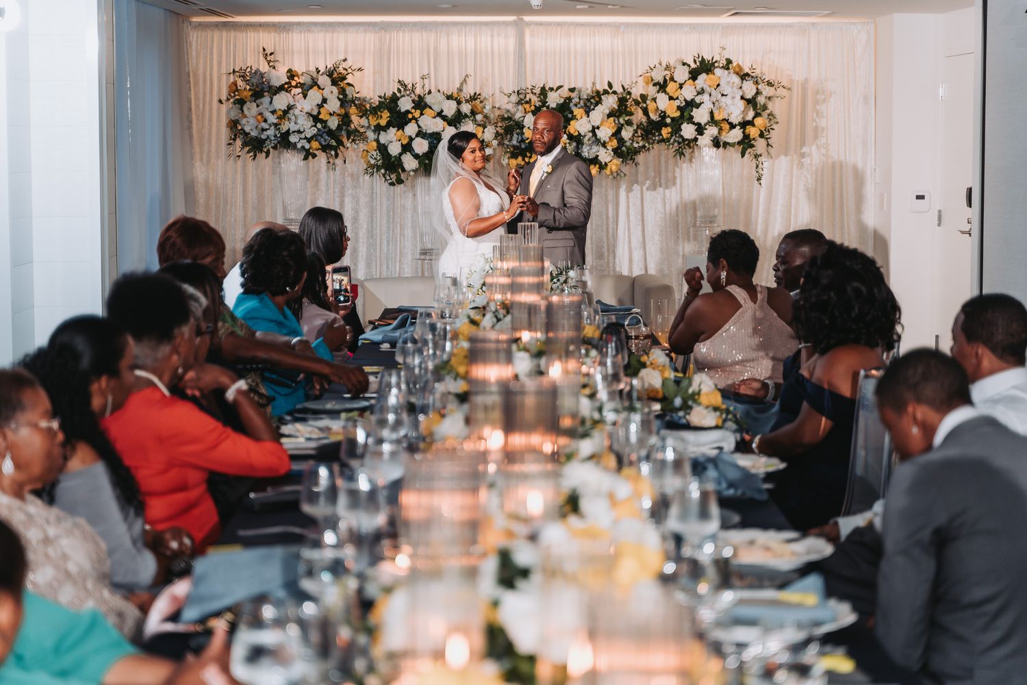 Wedding reception dinner setup with floral arch and elegant table settings.