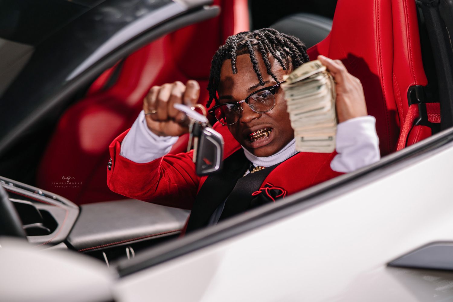 Someone in a red jacket sitting in a luxury car showing off money stacks.