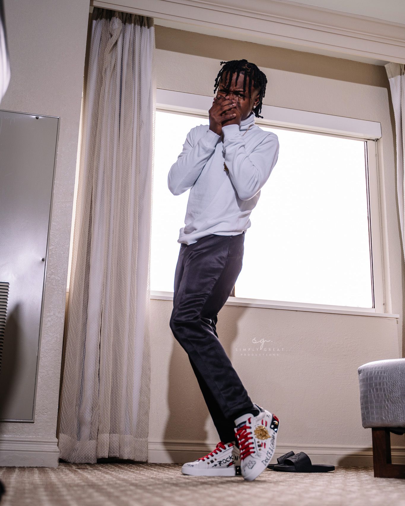 Person in casual attire and sneakers poses expressively by window.