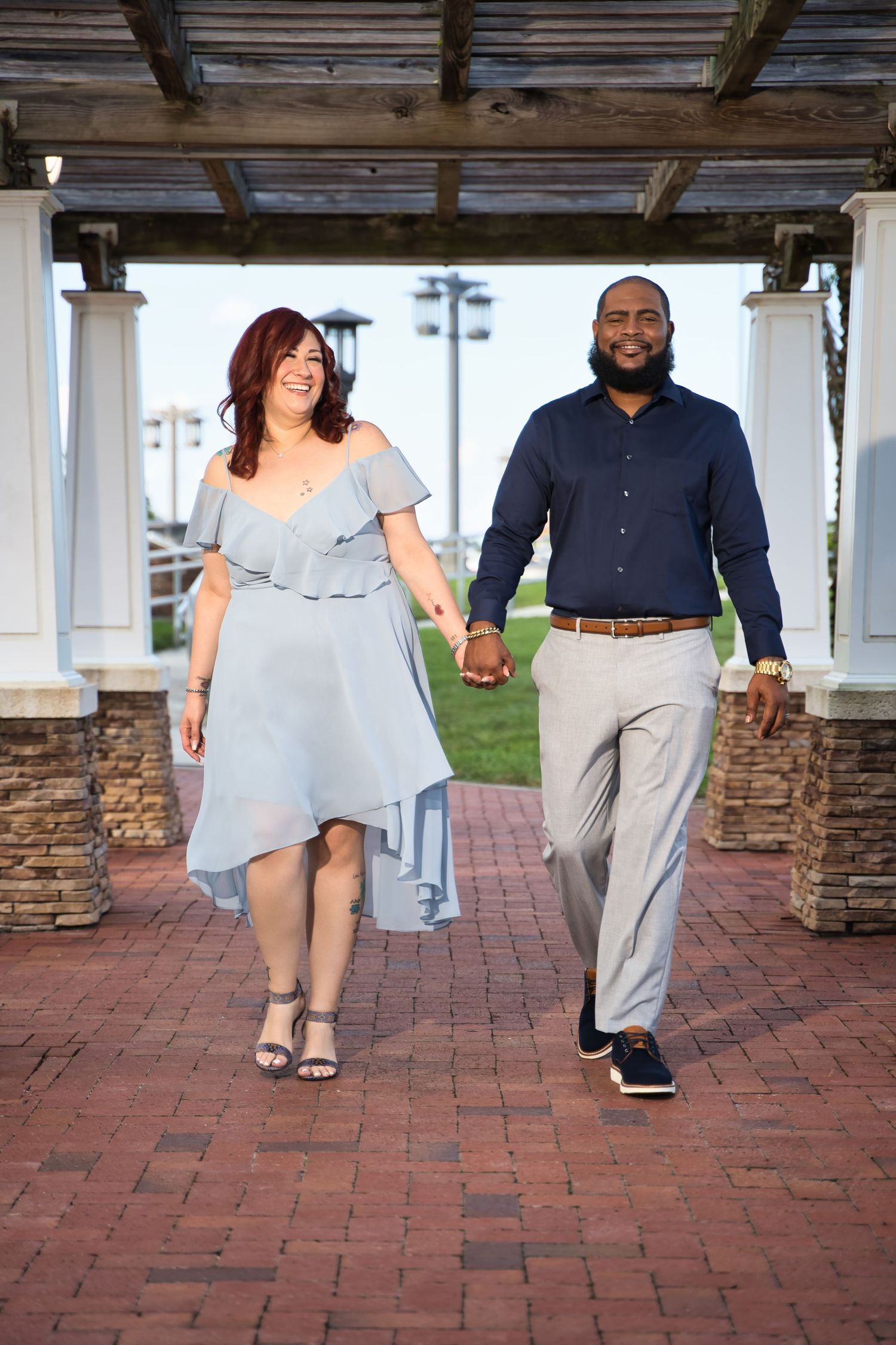 A couple walking hand in hand under a covered walkway wearing coordinated blue and grey outfits.
