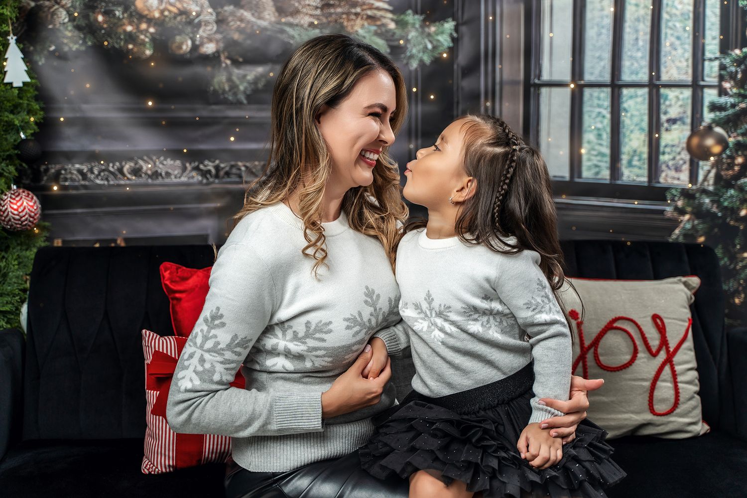 Two people in matching winter sweaters share a candid laughing moment on a holiday-decorated bench.