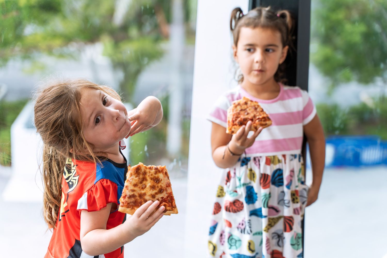 Two children eating pizza slices during an outdoor party event.