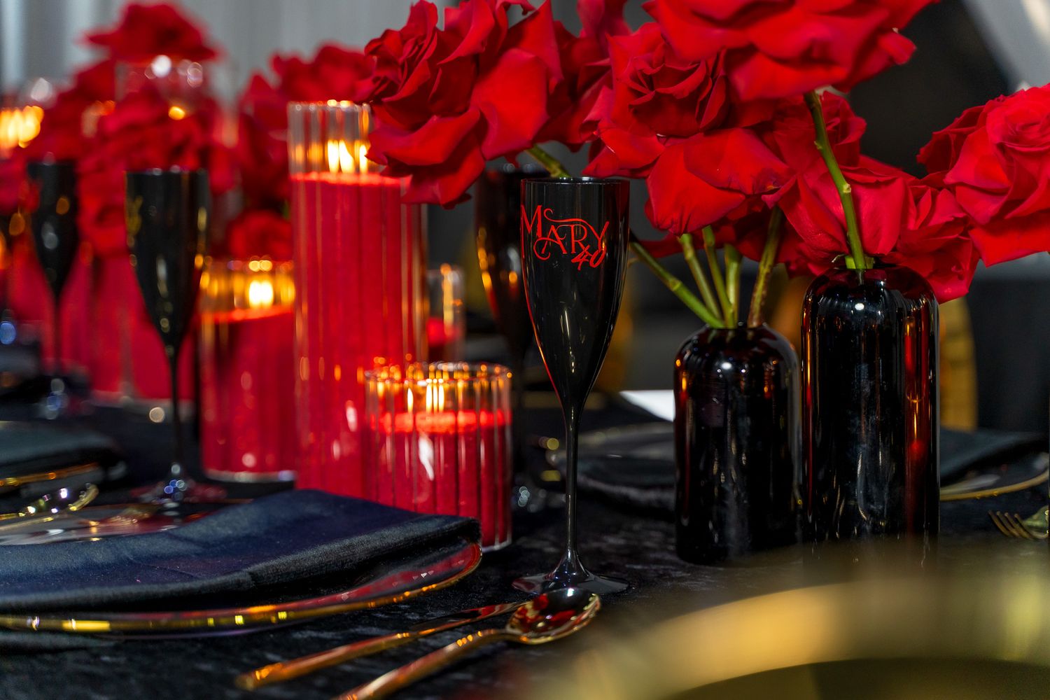 Dramatic table setting with red roses in black vases and glowing red candles.