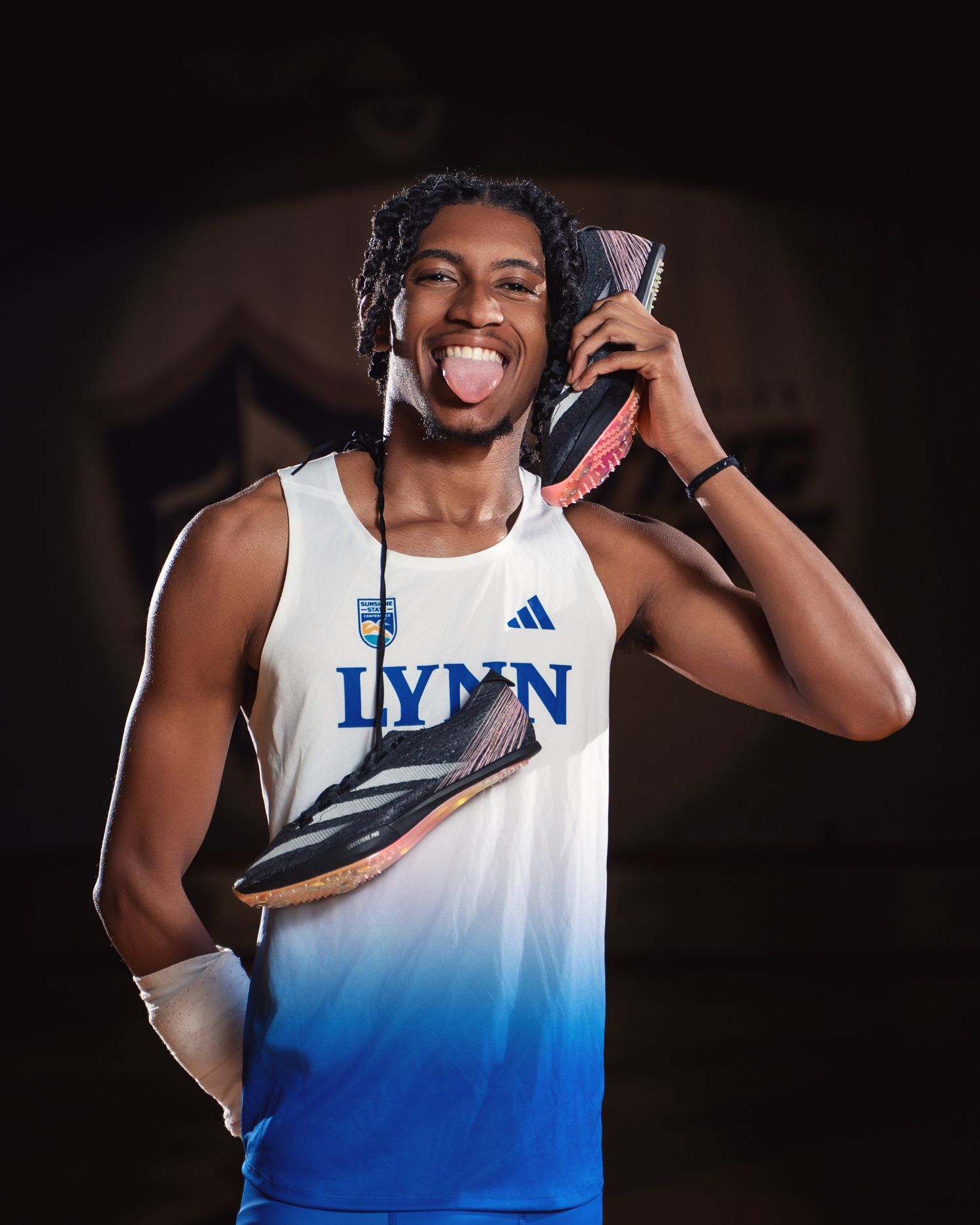 Athlete in white and blue gradient uniform showing enthusiasm while holding up athletic shoes.