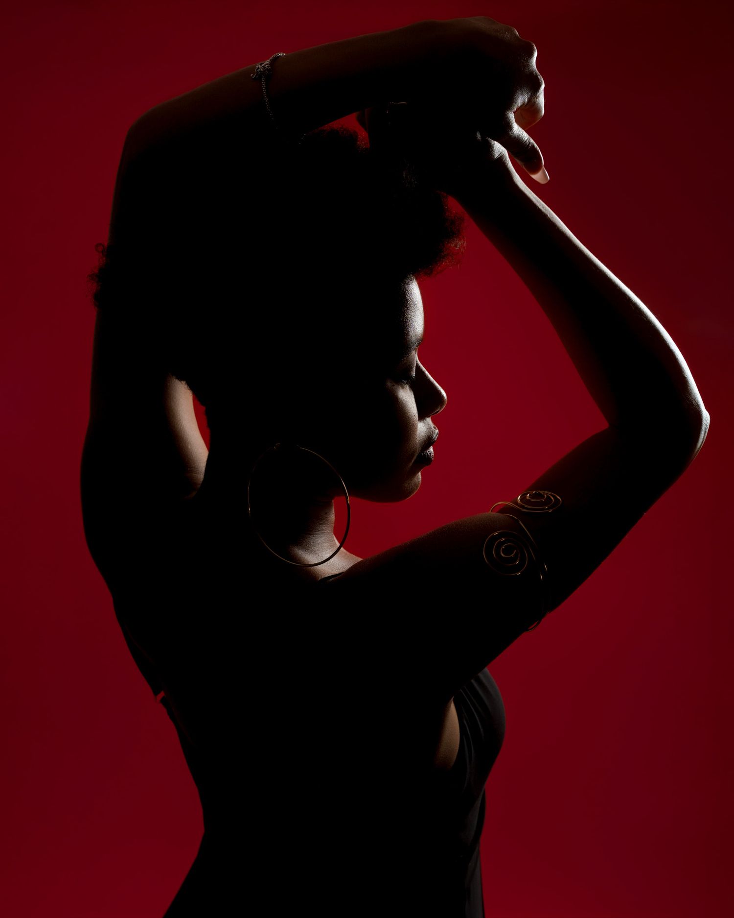 Silhouette portrait with dramatic lighting against red backdrop.