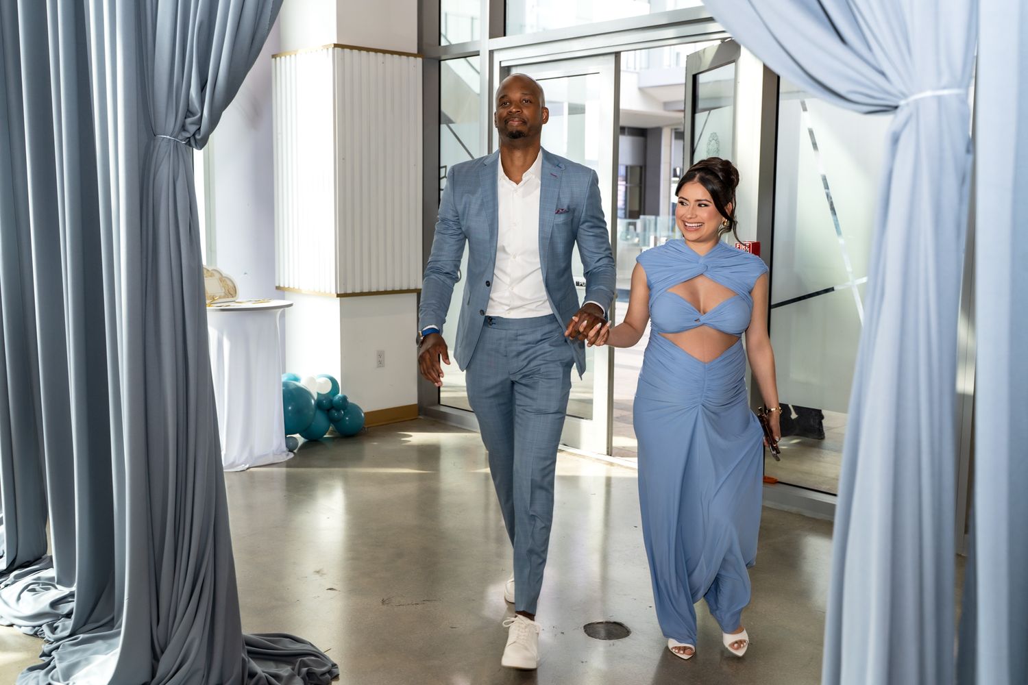 Couple walking hand in hand through curtained doorway at baby shower venue.