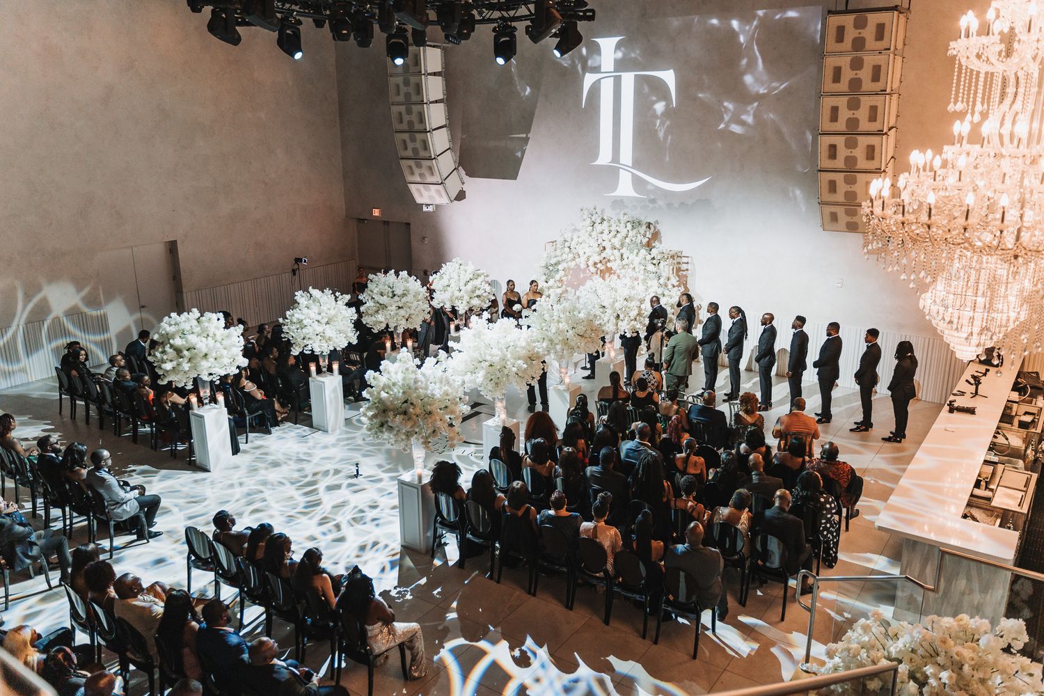 Aerial view of a wedding ceremony with white floral decorations and guests seated in black chairs.