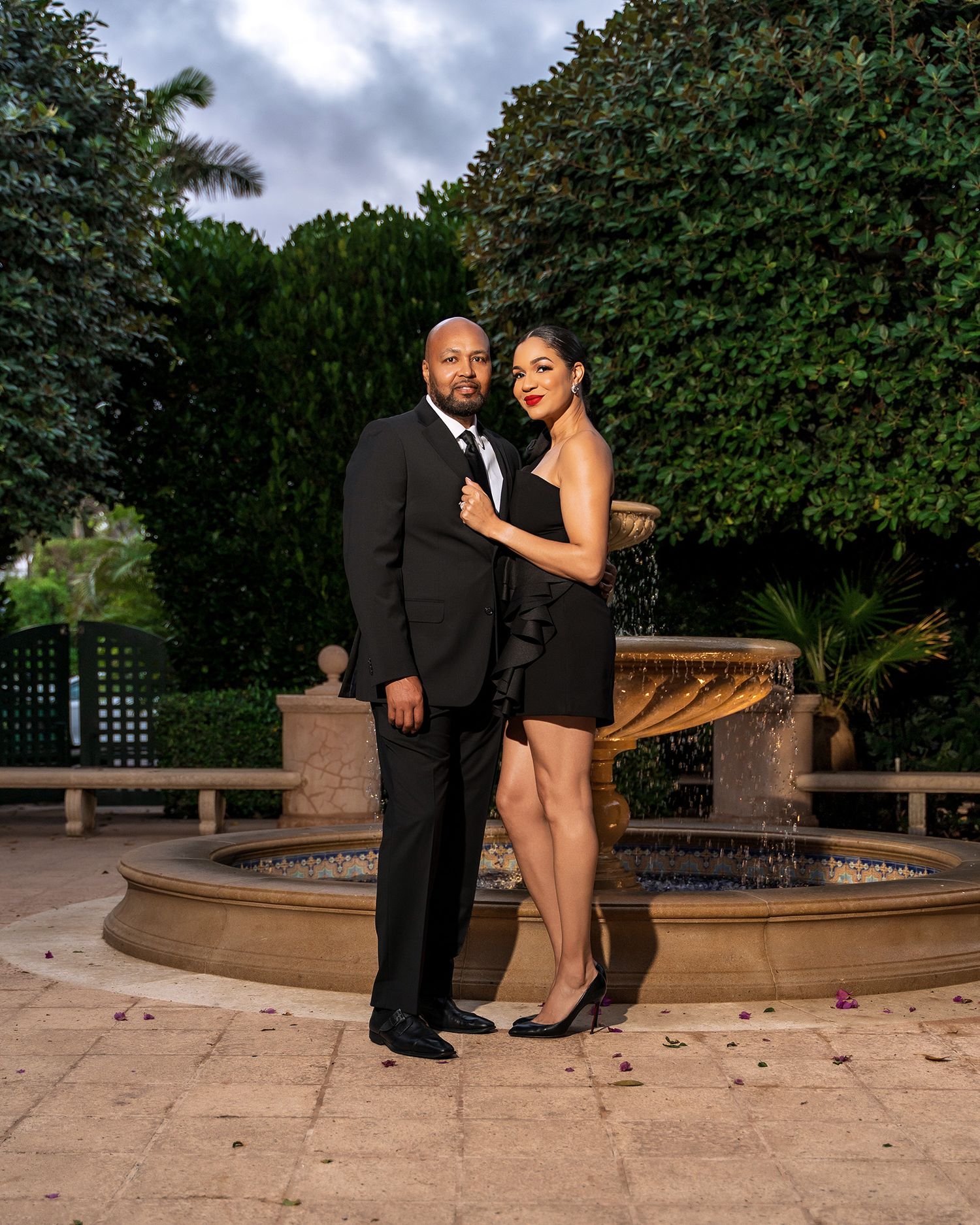 Elegant couple poses by outdoor fountain during formal event.