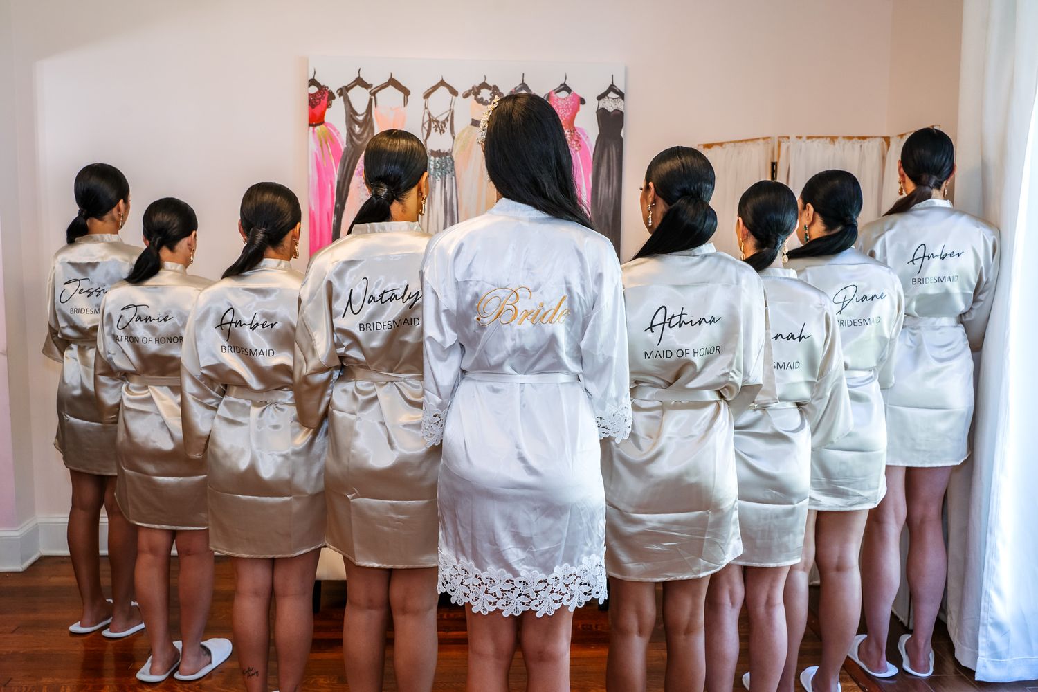 Bridesmaids showing off personalized robes from behind in a dressing room.