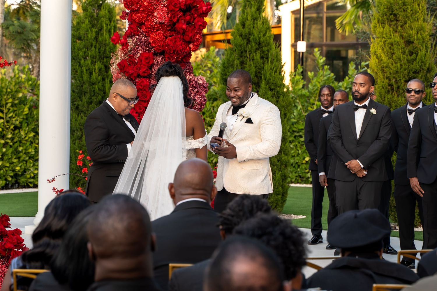 Wedding ceremony takes place outdoors with white pillars and red autumn foliage creating a romantic backdrop.
