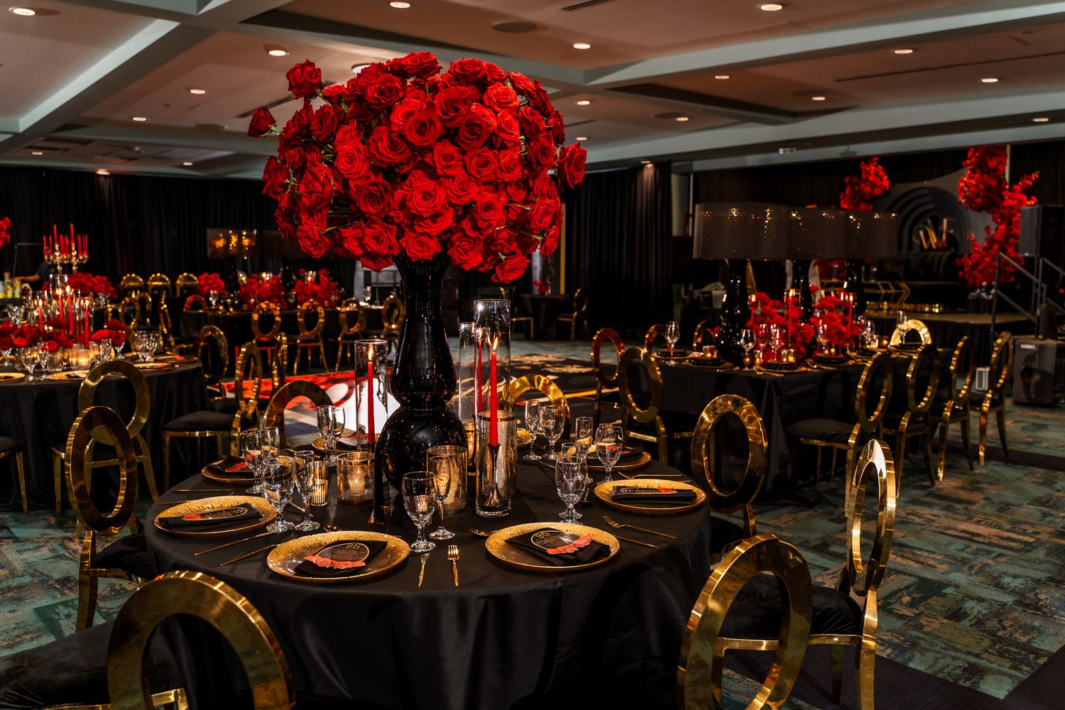 Elegant black and red wedding reception decor with dramatic red rose centerpieces and gold accented table settings.