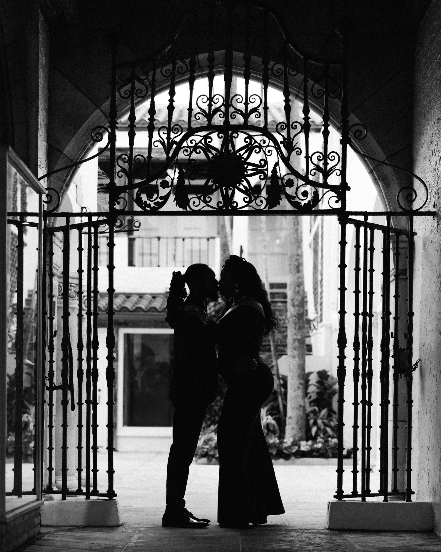 A silhouetted couple embracing in a romantic moment under an ornate arched gateway with wrought iron details.