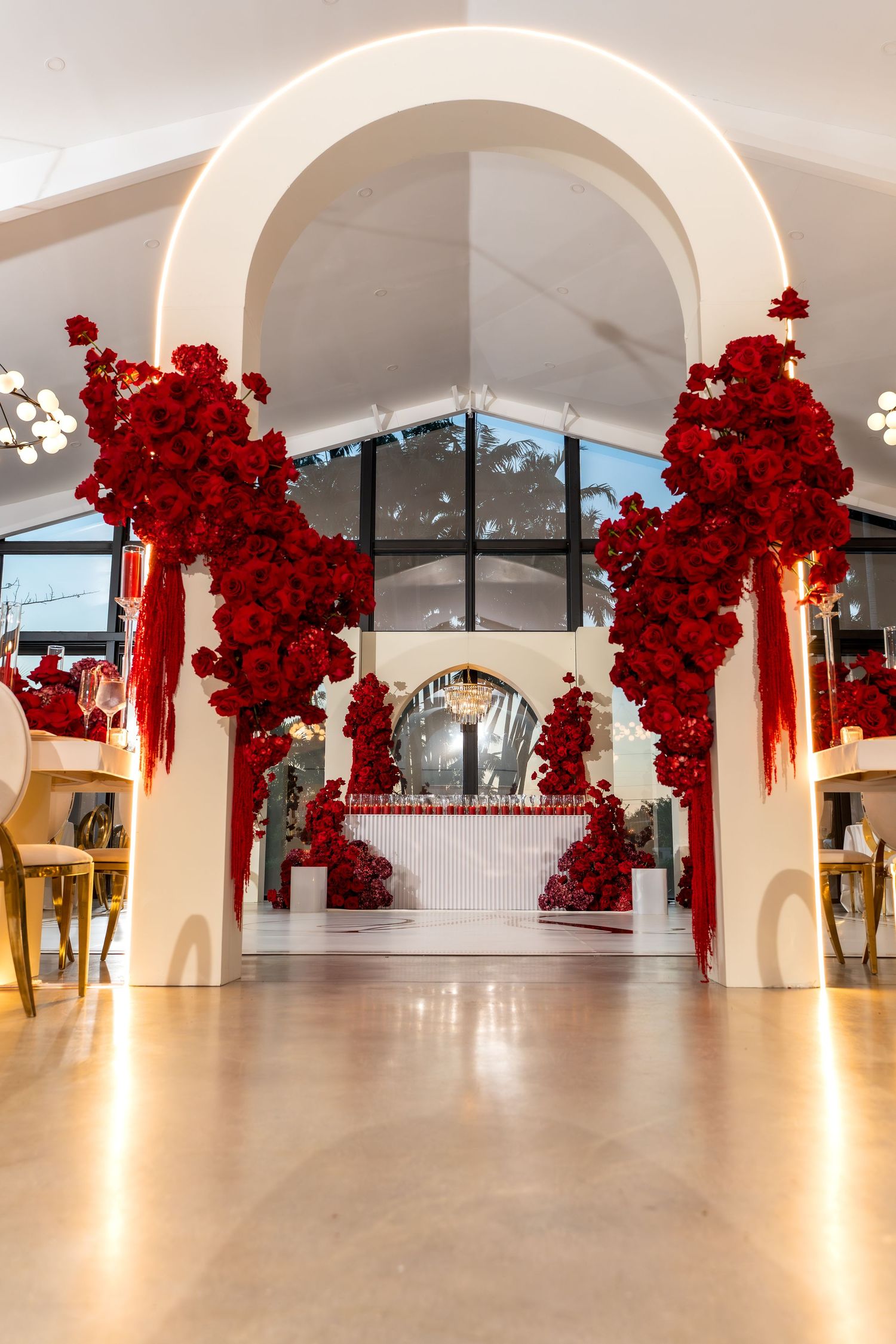 Modern event space decorated with dramatic red floral installations hanging from arched ceiling.