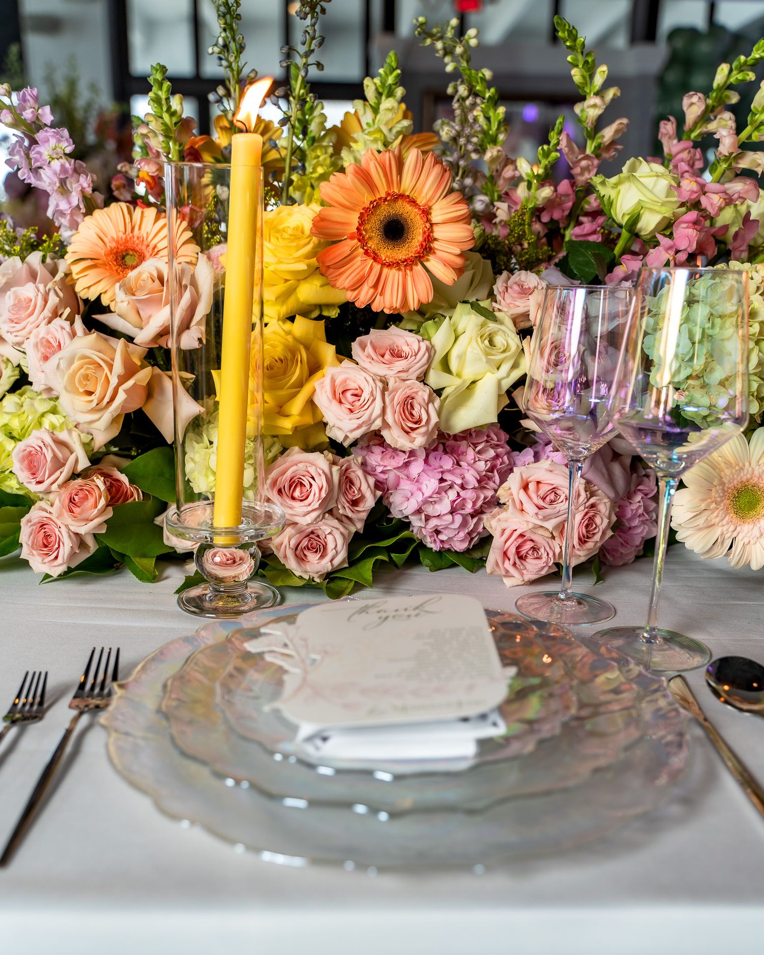 Elegant table setting with pink roses, orange gerberas, and yellow candles at a celebration.