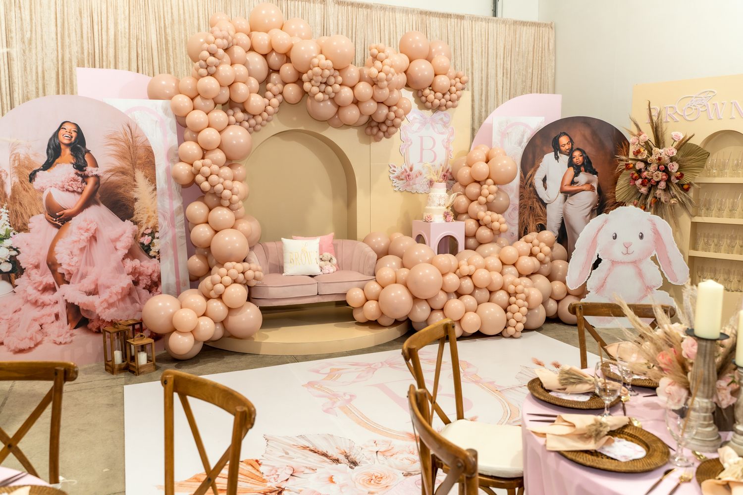Pink and peach balloon arch decorating an elegant baby shower setup with vintage furniture.