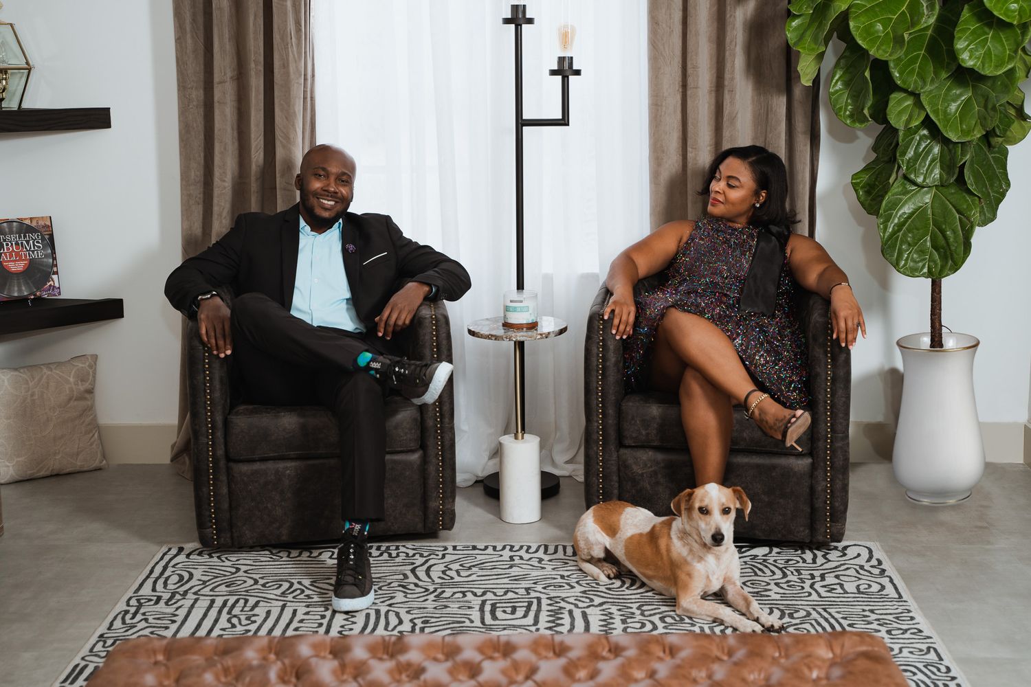 Stylish living room scene with couple in leather chairs and pet dog on geometric print rug.