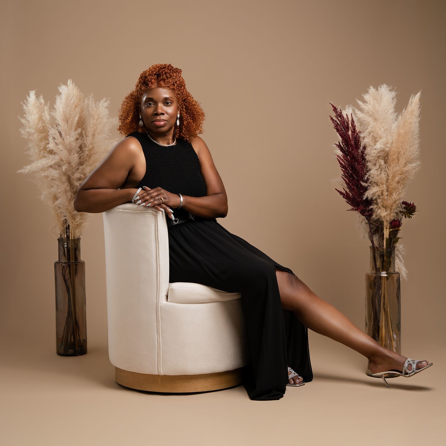 Elegant portrait in black dress seated on white chair with pampas grass decor.