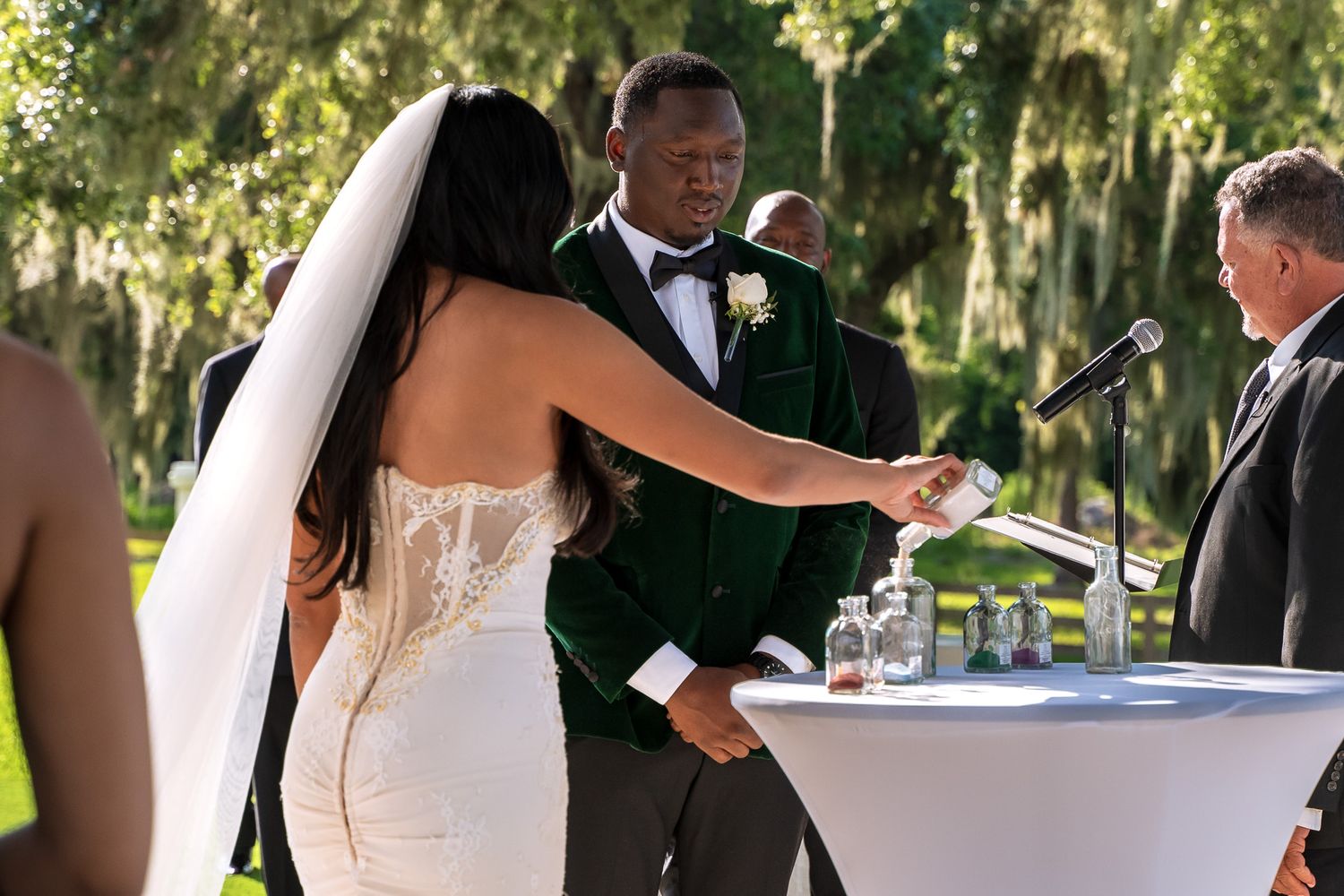 A wedding ceremony takes place outdoors under Spanish moss draped trees.