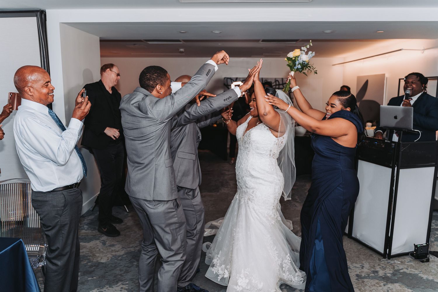Wedding party celebrating with raised arms on the dance floor during reception.