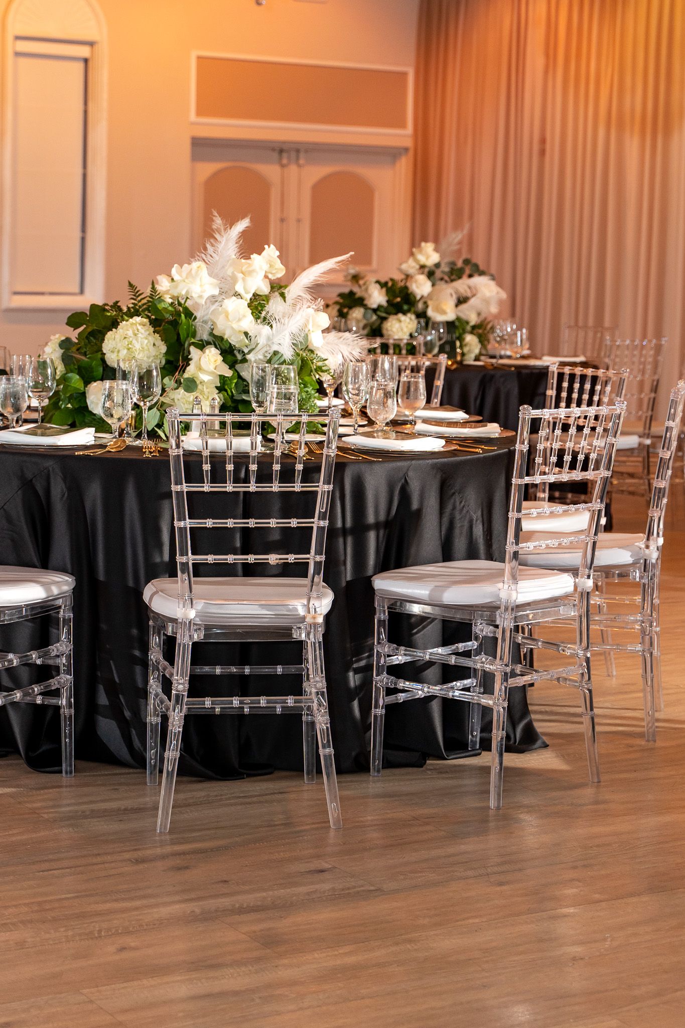 Elegant wedding reception table with black linens, white floral centerpieces and crystal chiavari chairs.