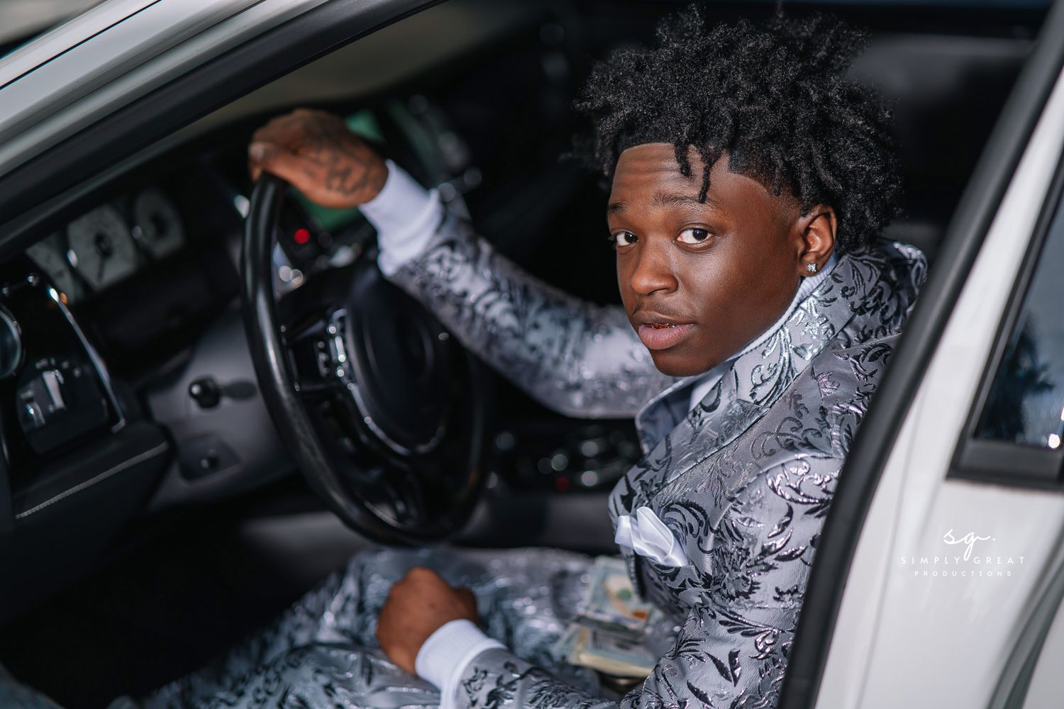 Person in gray patterned suit holding steering wheel of white car interior.