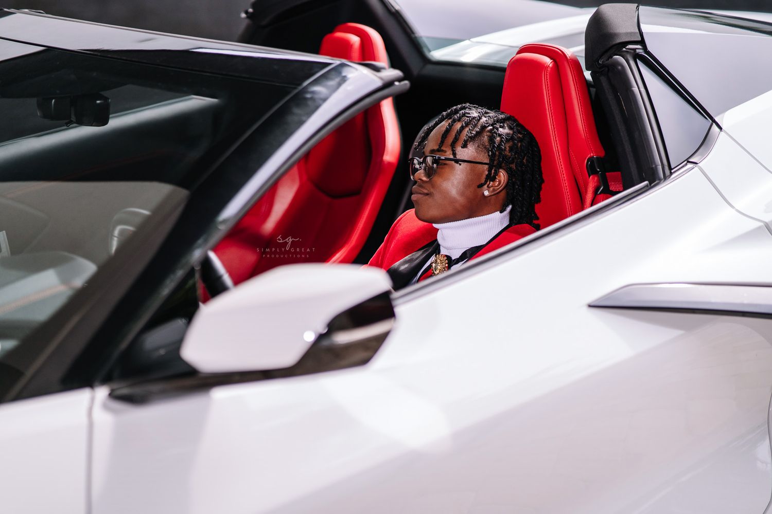 Someone sits in a white luxury car with red interior.