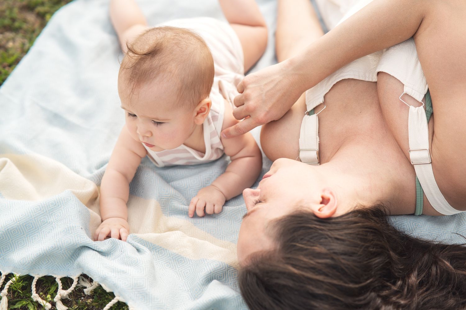 A baby and parent lie together on a white blanket in soft natural lighting.