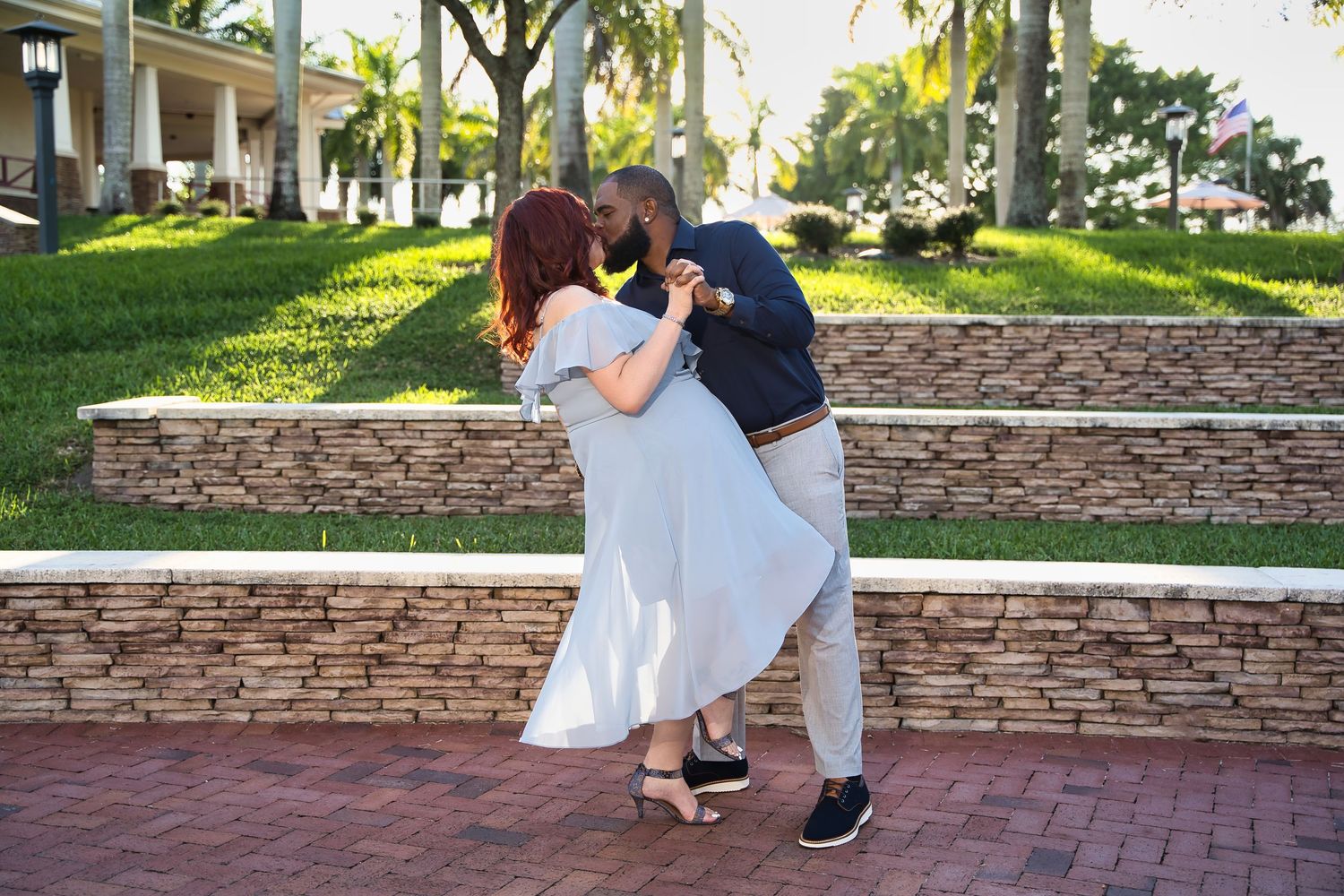 A couple in coordinated outfits share a romantic dip pose on a brick pathway.