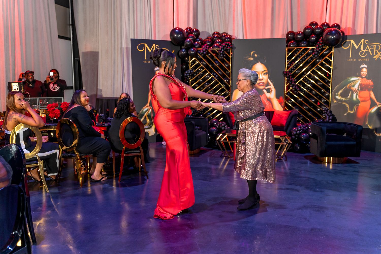Two guests dance together at an elegant event with decorative branded backdrop.