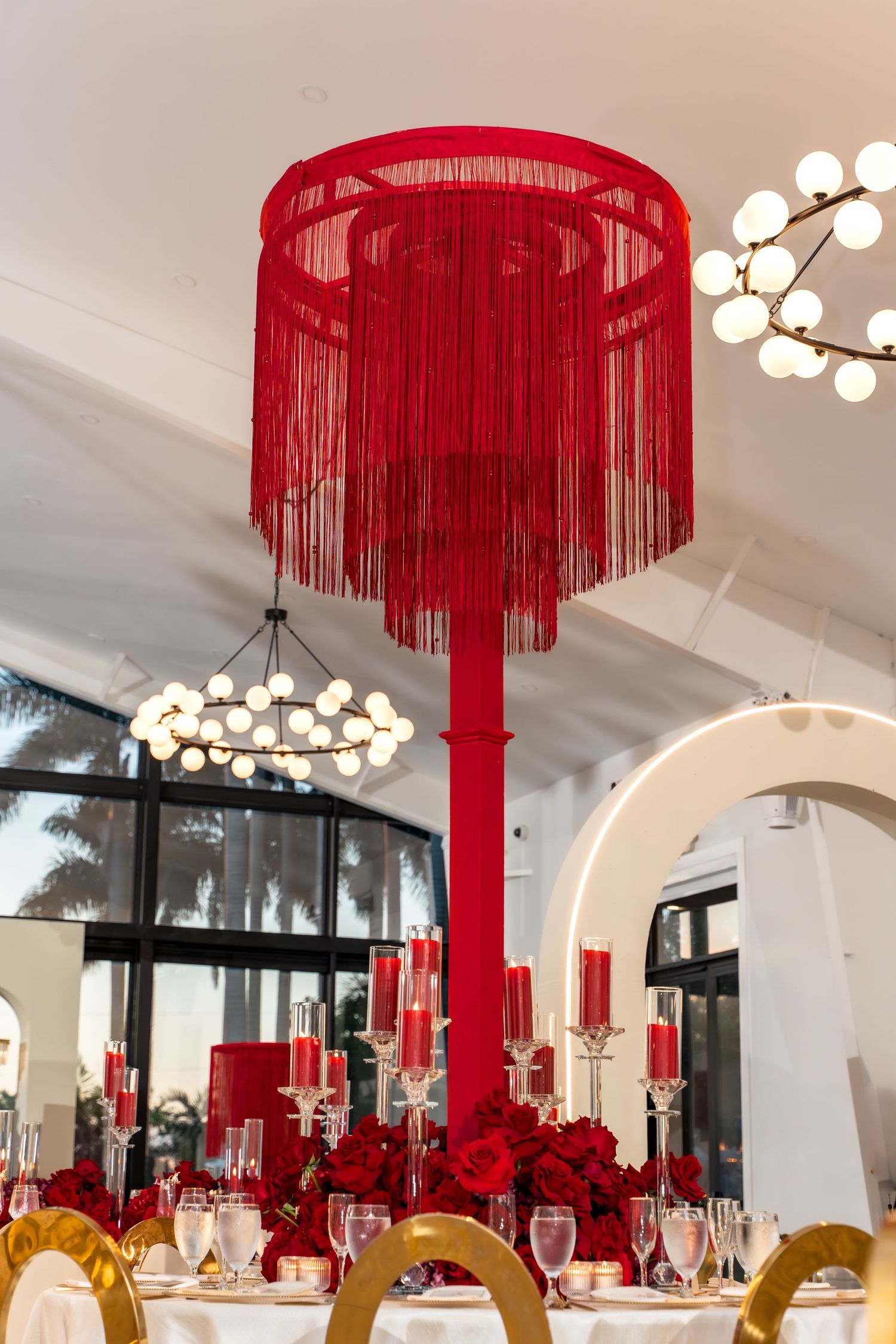 Modern reception venue with red chandelier decorations and spherical white light fixtures.