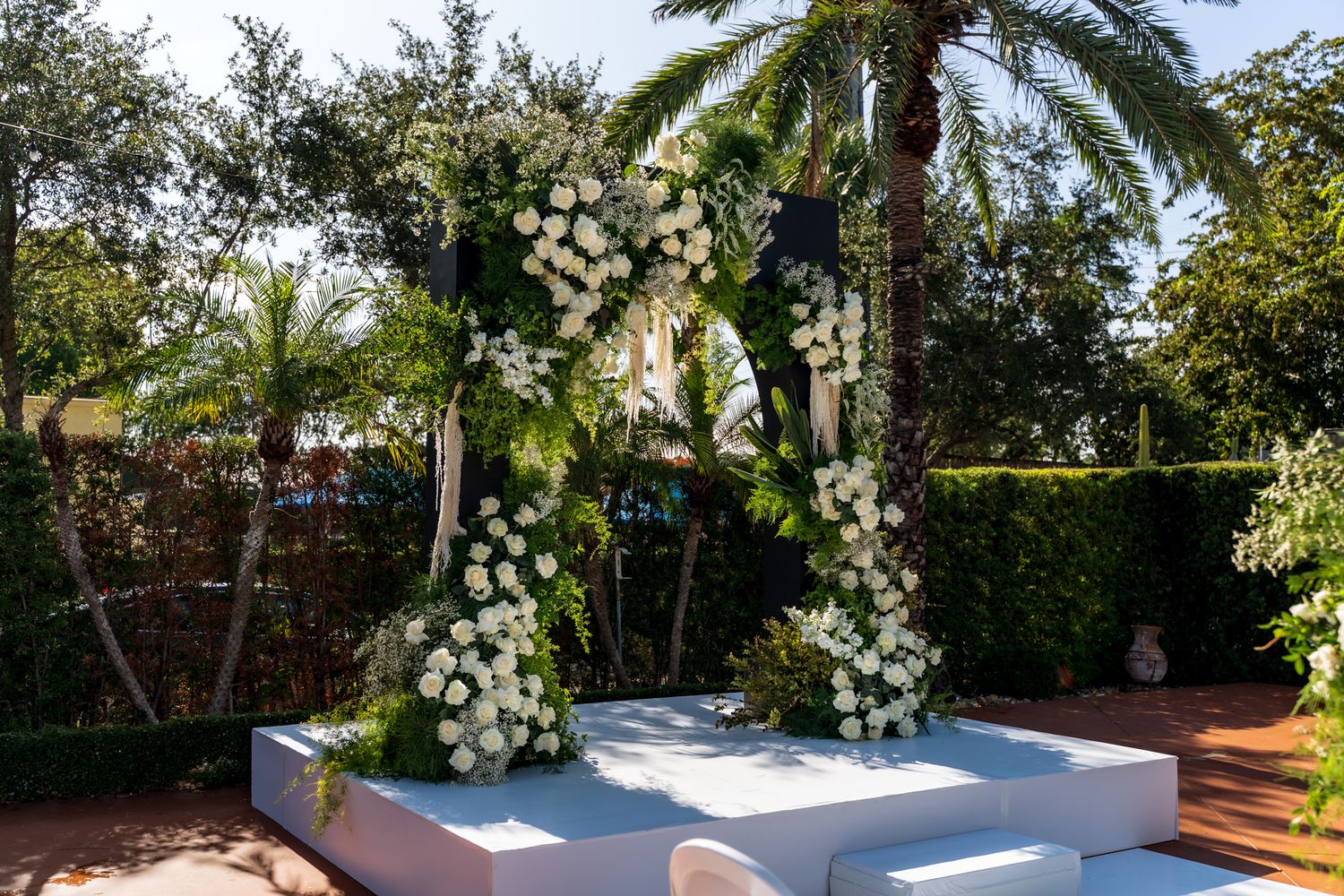 Wedding ceremony setup with white floral arches and seating arrangements in a lush garden setting.