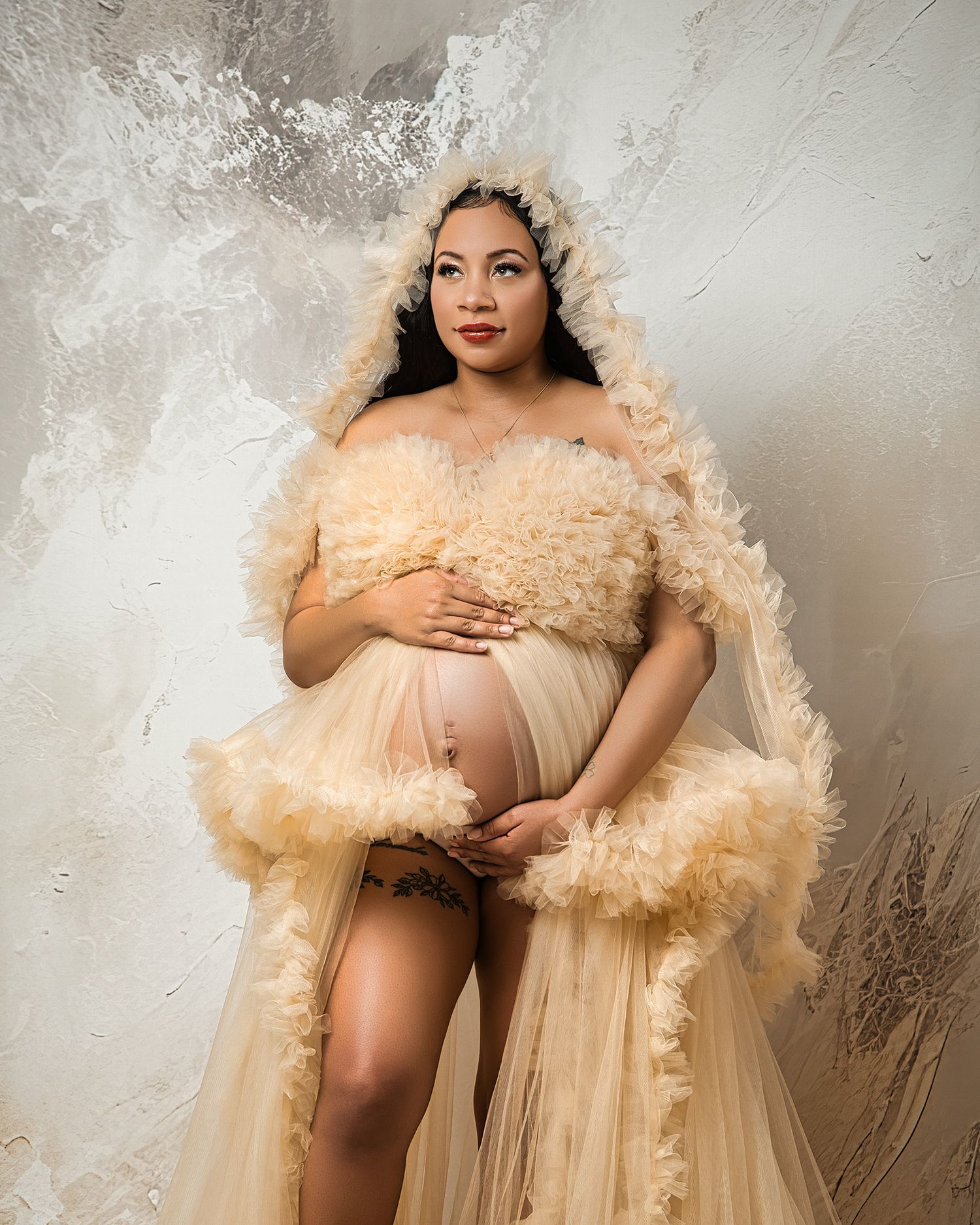 Dreamy maternity portrait with ruffled champagne dress against textured wall.