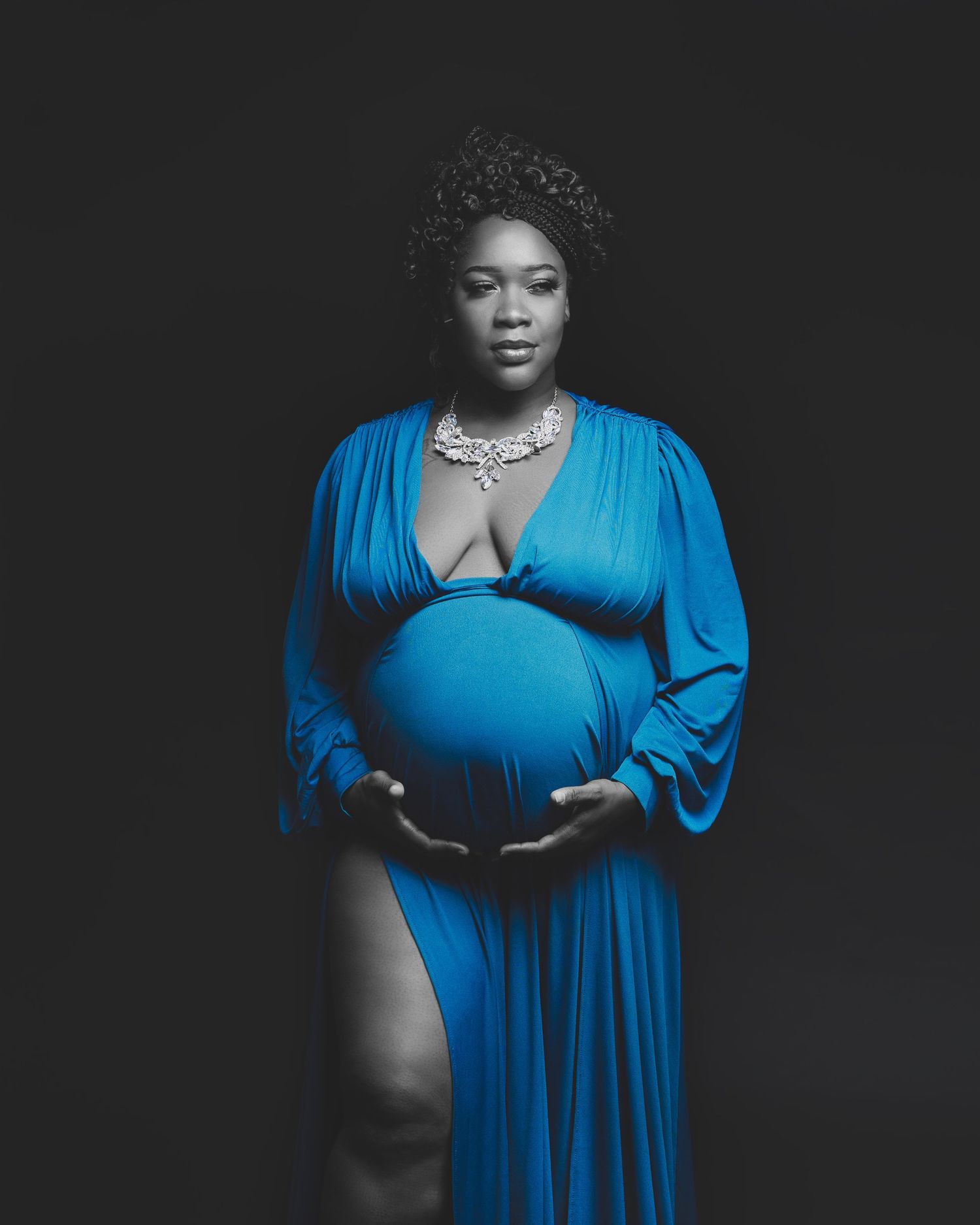 Artistic black and white maternity photo featuring a woman in blue dress wearing statement jewelry.