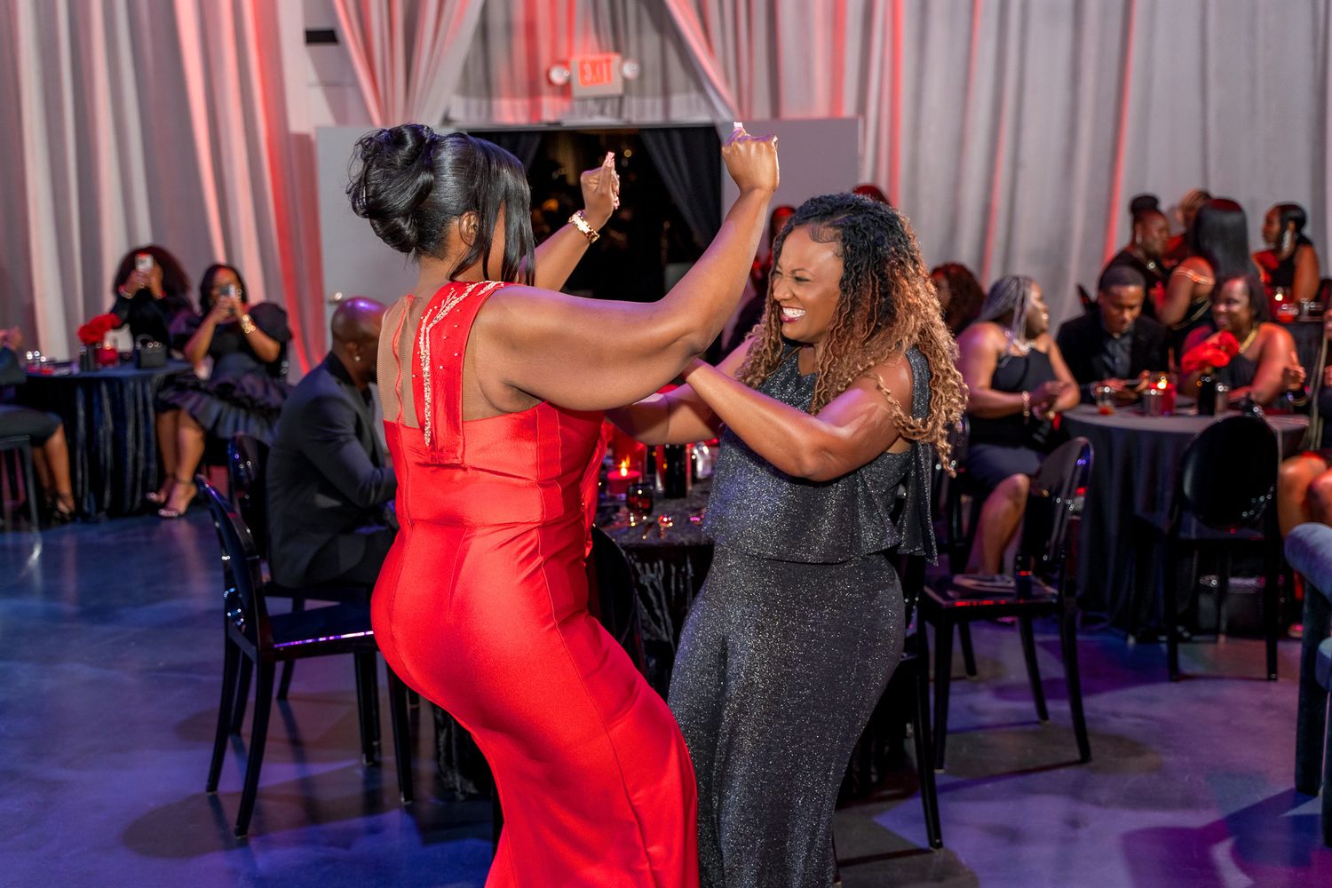 Two attendees share a joyful dance moment at an indoor celebration with ambient lighting.