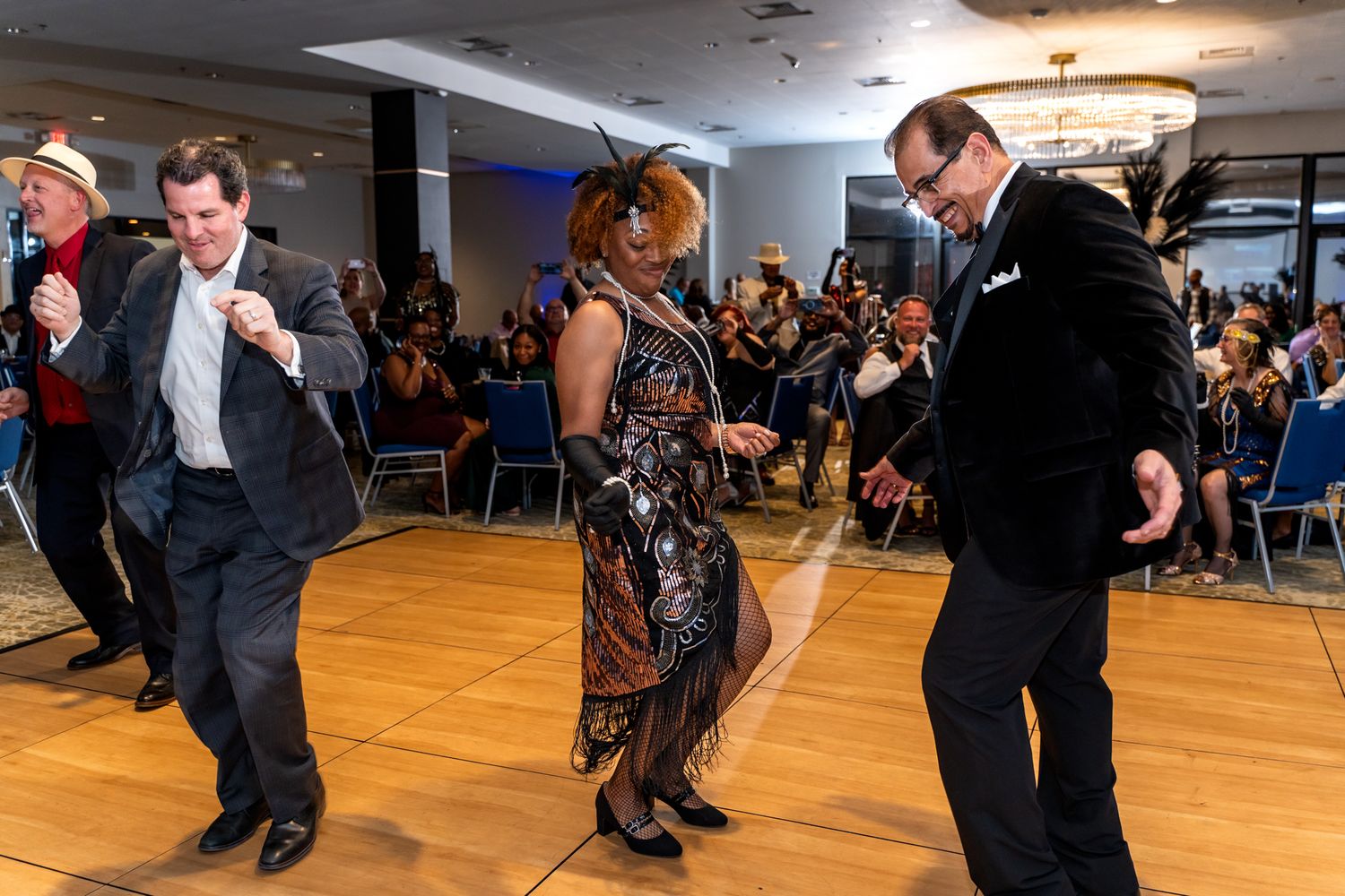People dancing enthusiastically on a wooden dance floor at a formal party.