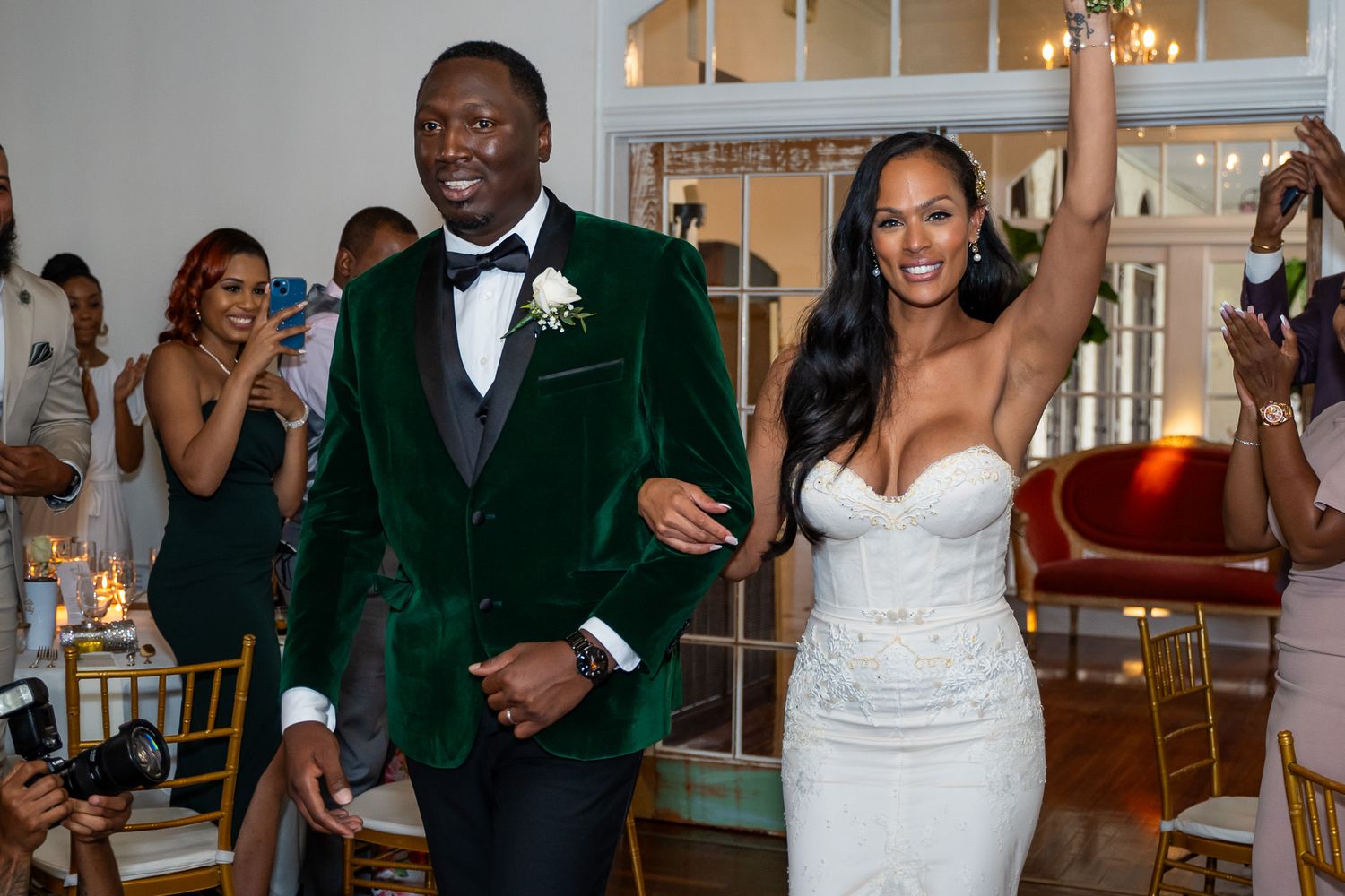 Newlyweds make joyful entrance at wedding reception in green velvet and white gown.