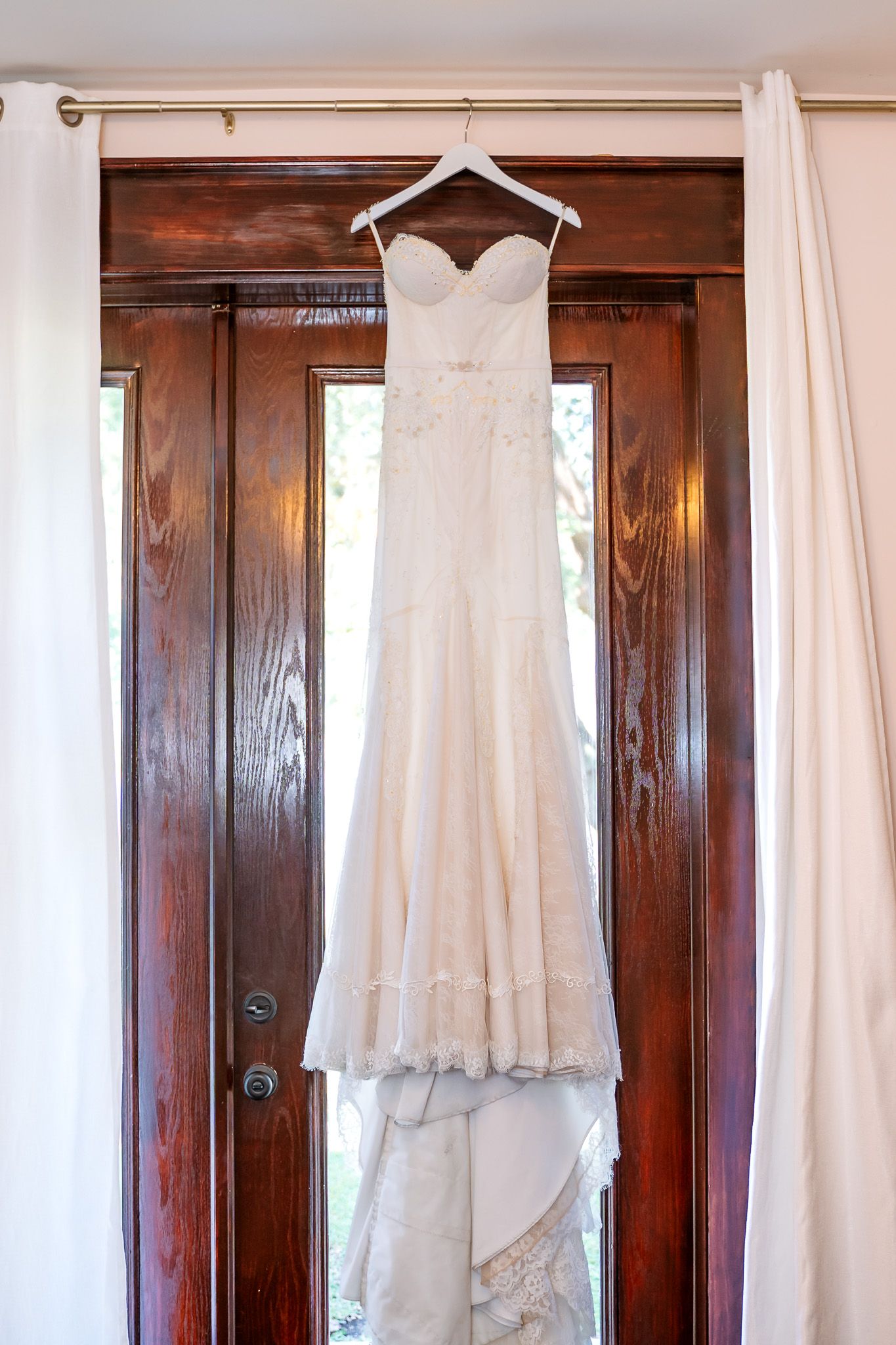 White wedding gown hanging against wooden door in elegant dressing room.