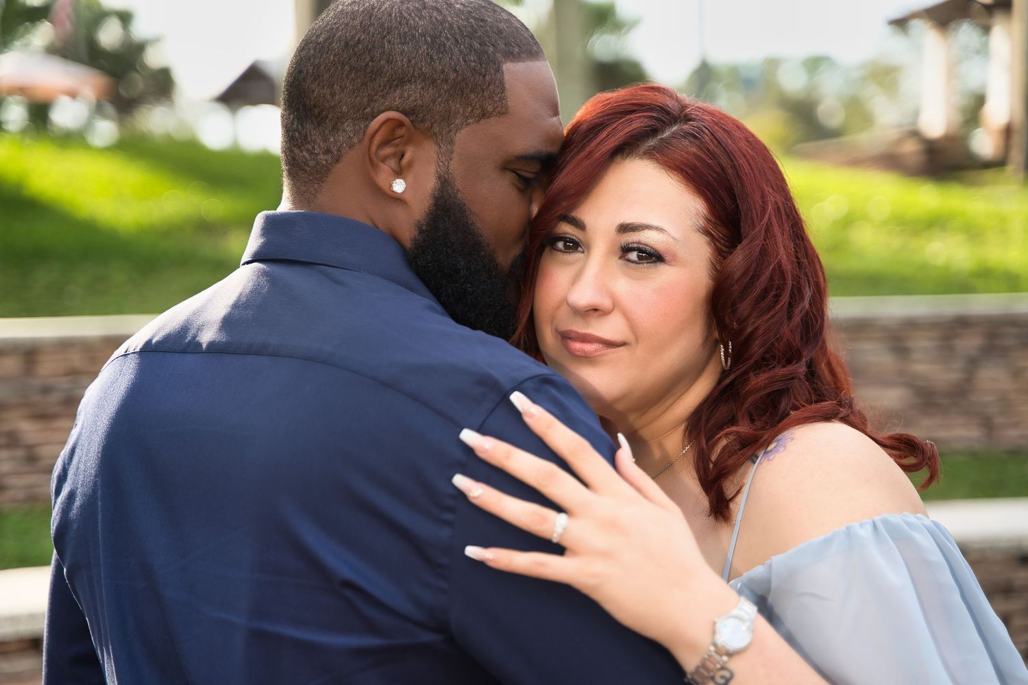 A couple in formal attire share an intimate moment outdoors during an engagement photoshoot.