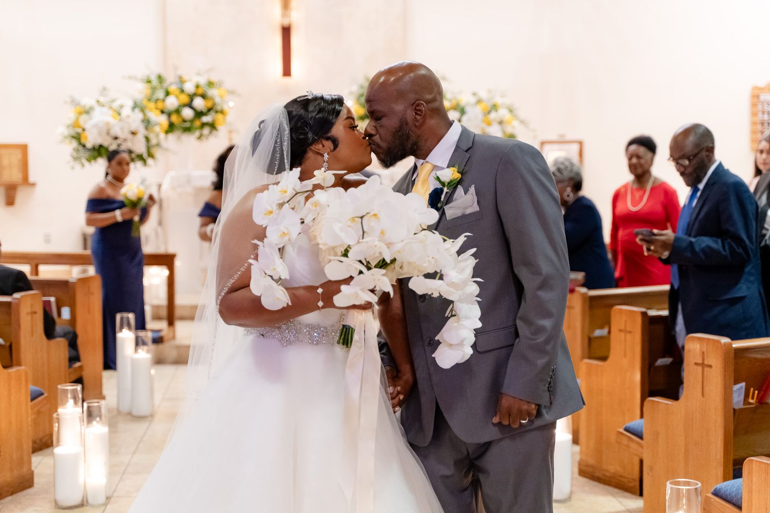 Newlyweds share first kiss at altar with white floral arrangements and church decor.