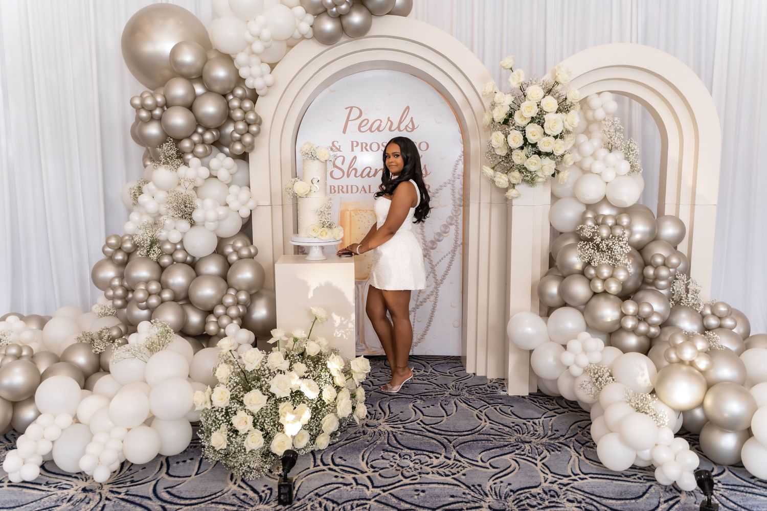 Elegant white and silver balloon garland arch installation with floral arrangements against a light backdrop.