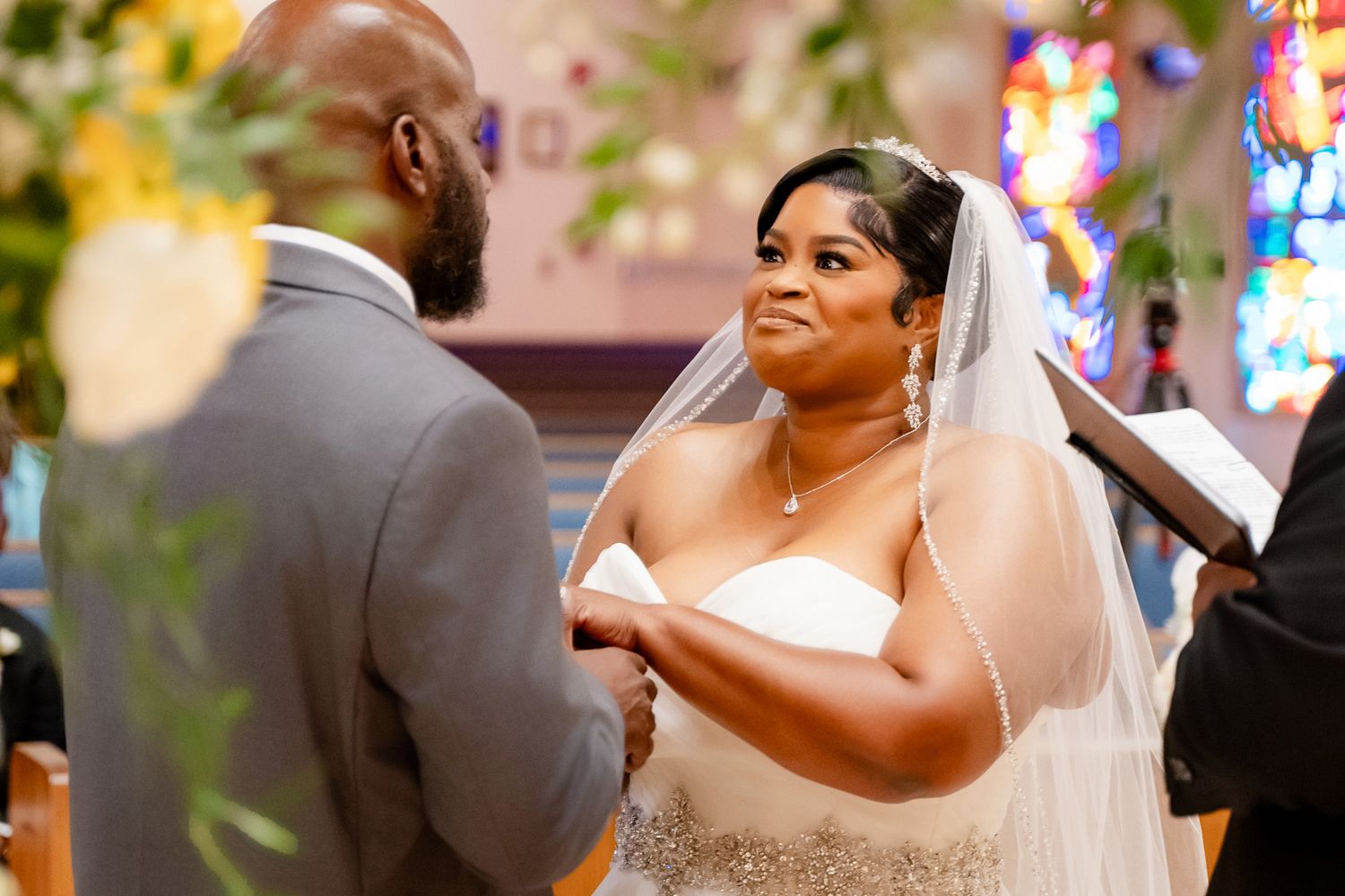 Intimate moment during wedding ceremony with bride in white dress exchanging vows at church altar.