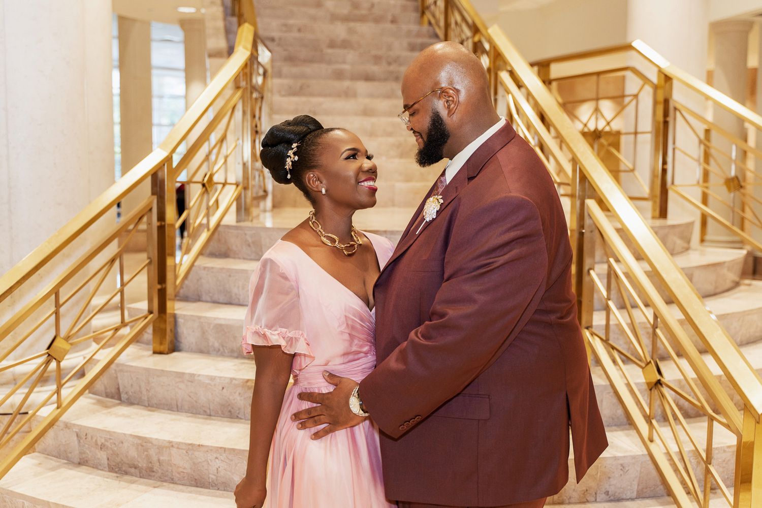 A couple shares a joyful moment on an elegant staircase with gold railings.