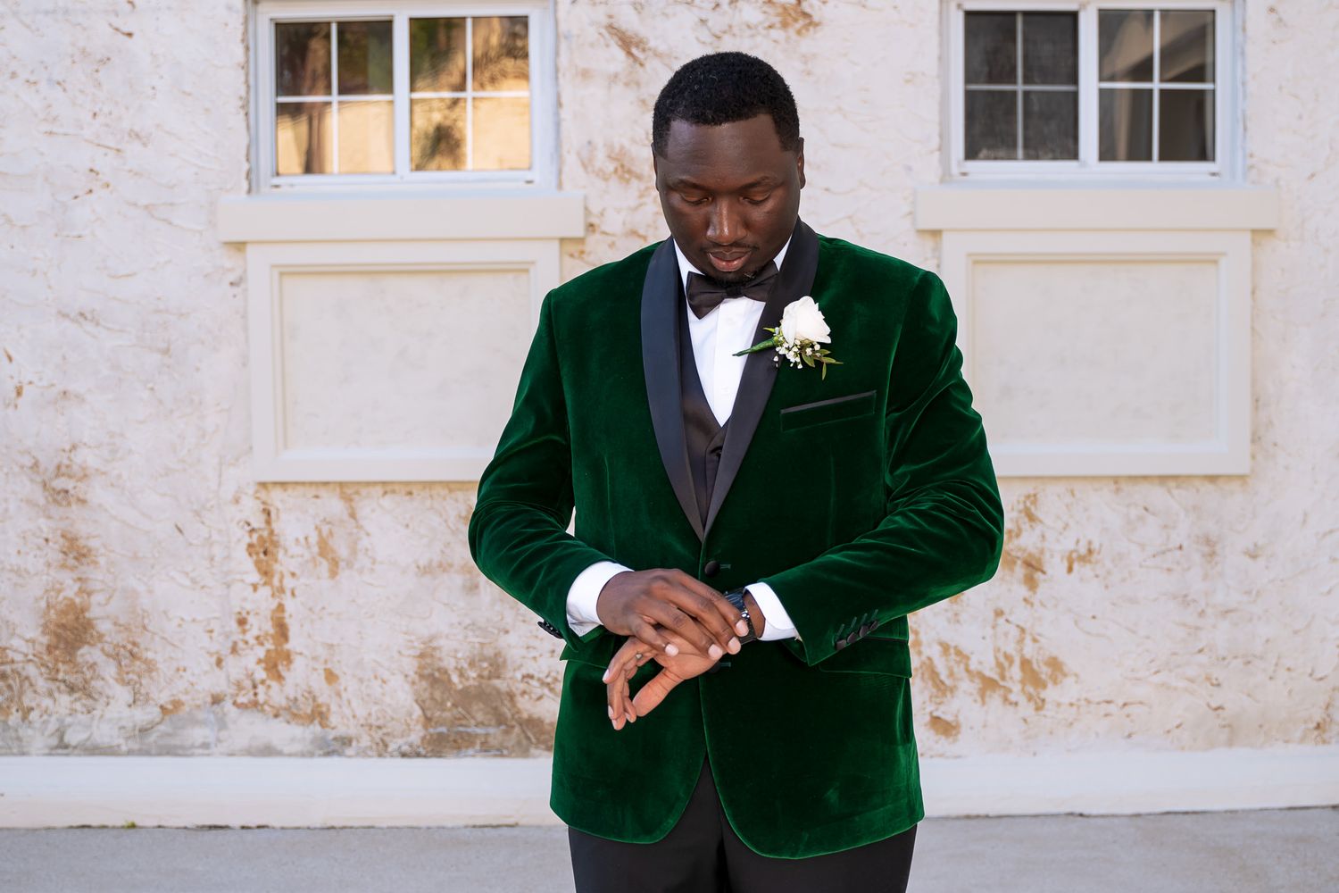 Groom checks his watch while wearing luxurious green velvet tuxedo.