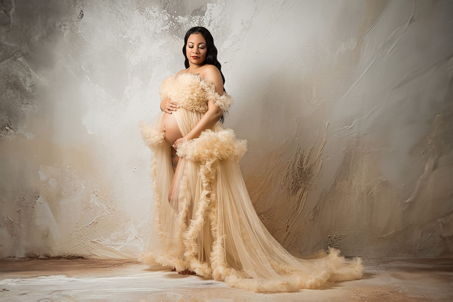 Elegant maternity photo featuring flowing beige tulle gown against neutral backdrop.